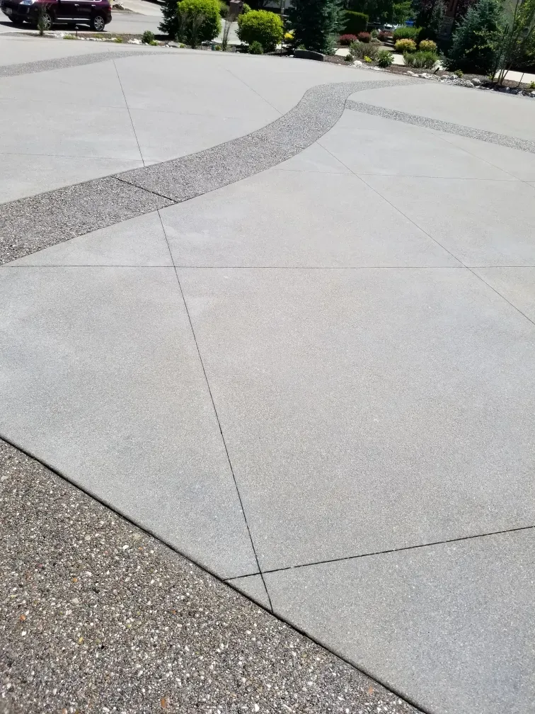 Residential concrete driveway with a decorative exposed-aggregate border curving through a broom-finished surface.