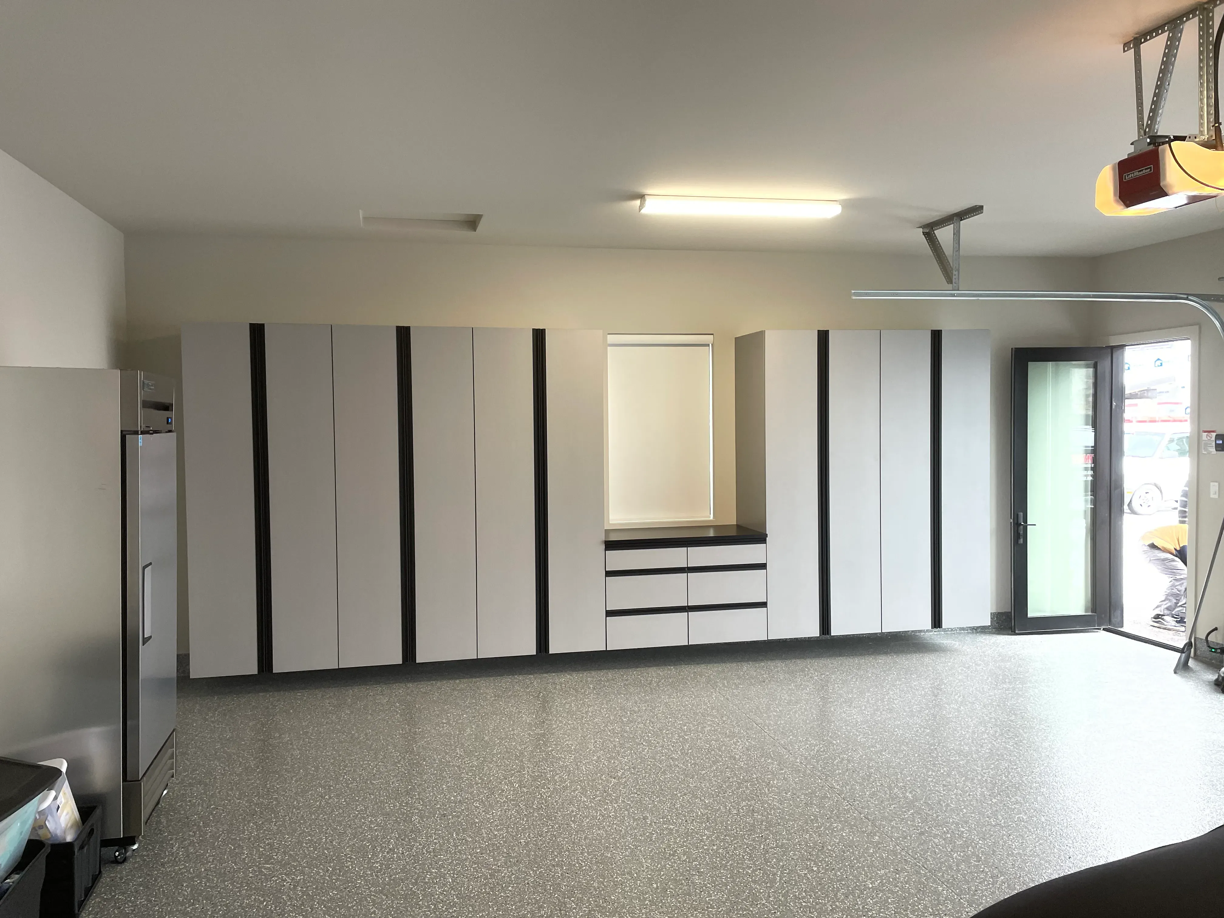 Full wall of light gray garage storage cabinets with a coated floor.