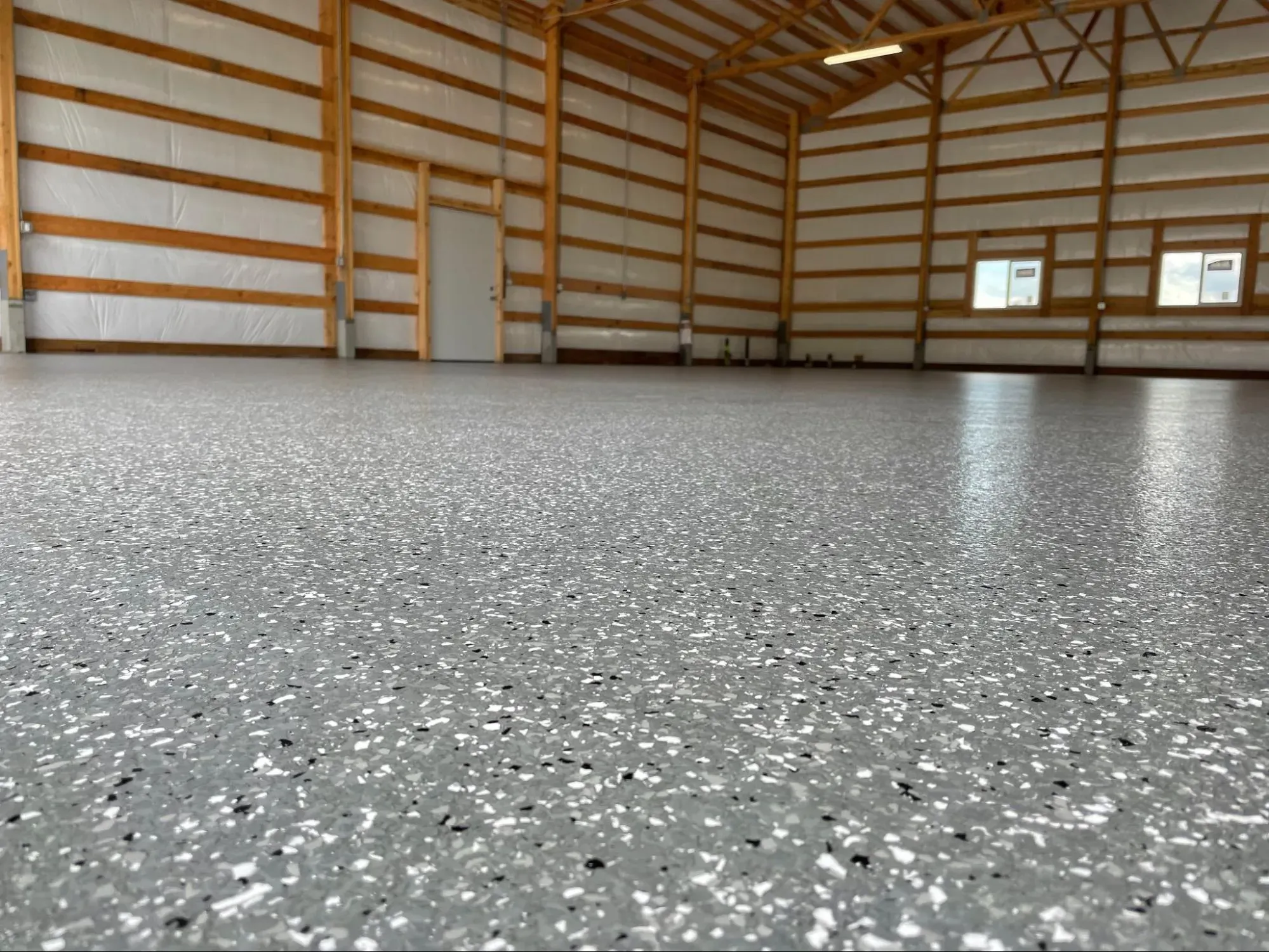 Interior of a large pole-building shop with a light gray textured protective coating covering the full concrete slab.