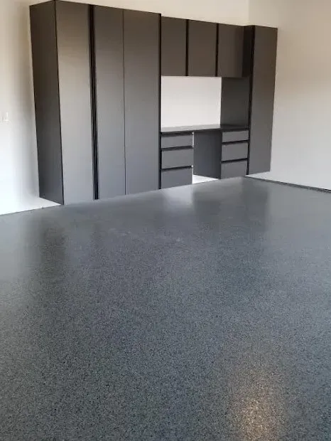 Custom gray garage storage cabinets with a built-in workbench above a fresh gray flake-coated concrete floor.