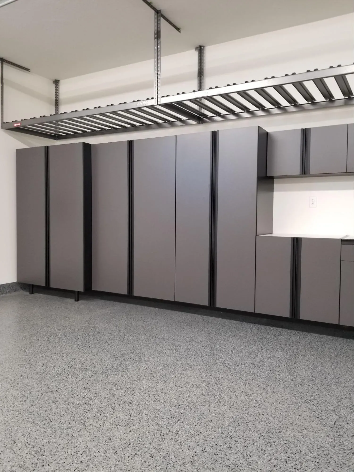 Finished garage interior with wall-to-wall storage cabinets, an overhead storage rack, and a speckled epoxy flake floor.