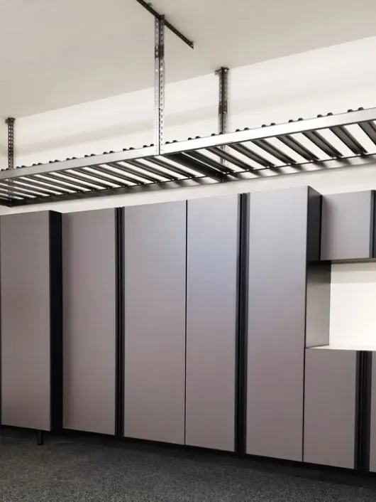 Heavy-duty overhead storage rack mounted above a wall of gray garage cabinets.