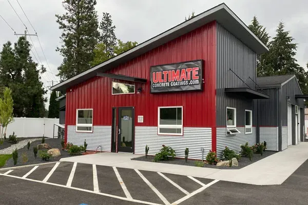The Ultimate Concrete Coatings showroom — a red and corrugated-metal building in Rathdrum, Idaho with a lit sign.